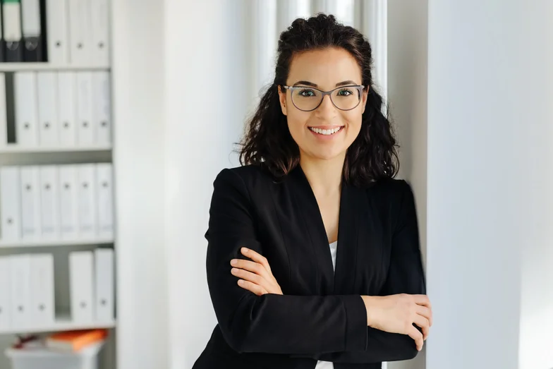 Beraterin mit verschränkten Armen und Brille in einem Büro.